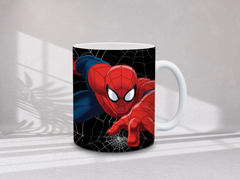 May include: White ceramic mug featuring a vibrant illustration of Spider-Man in his iconic red and blue suit. The superhero is depicted against a black background with white spiderwebs. The mug has a white handle.