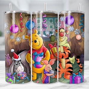 May include: A stainless steel tumbler featuring a festive scene with Winnie the Pooh, Tigger, Eeyore, and Piglet. The design includes Christmas decorations, gifts, and a cozy interior setting. The tumbler has a clear straw and is designed for cold beverages.