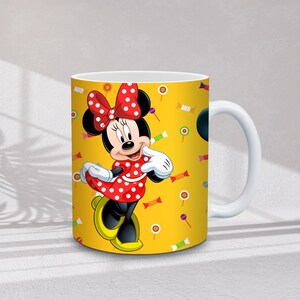 Może przedstawiać: Biały ceramiczny kubek z Minnie Mouse w czerwonej sukience w kropki i kokardą. Kubek ma ż&oacute;łte tło z ilustracjami cukierk&oacute;w i lizak&oacute;w. Uchwyt jest biały.