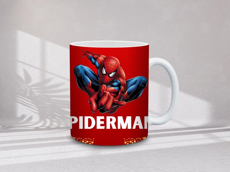May include: White ceramic mug featuring a vibrant image of Spider-Man in a dynamic pose against a red background. The word "SPIDERMAN" is printed in white. The mug has a white handle and a gold star pattern at the bottom.