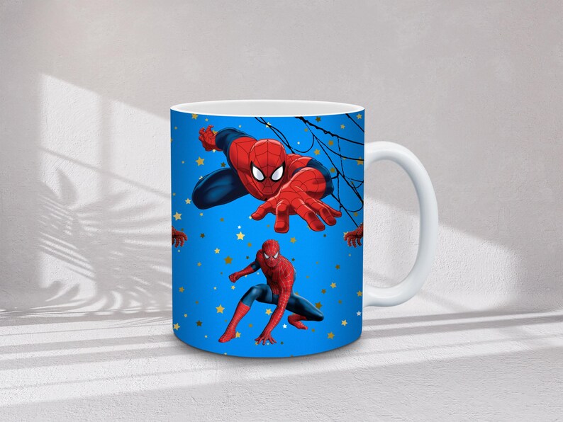 May include: White ceramic mug featuring Spider-Man in action poses against a blue background with gold stars. The superhero is depicted in his classic red and blue suit, with web details.