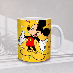 Może przedstawiać: Biały ceramiczny kubek z kresk&oacute;wkowym wizerunkiem Myszki Miki na ż&oacute;łtym tle z cukierkami i konfetti. Myszka Miki ma na sobie czerwone szorty, ż&oacute;łte buty i białe rękawiczki. Kubek ma biały uchwyt.