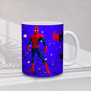 May include: White ceramic mug featuring a vibrant illustration of Spider-Man in his iconic red and blue suit. The design includes a spider web and spider graphics against a blue background. The mug has a white handle.