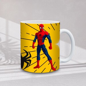 May include: White ceramic mug featuring a vibrant yellow background with a Spider-Man design. The design includes a Spider-Man figure in a red and blue suit, along with black spider silhouettes and web-like lines.