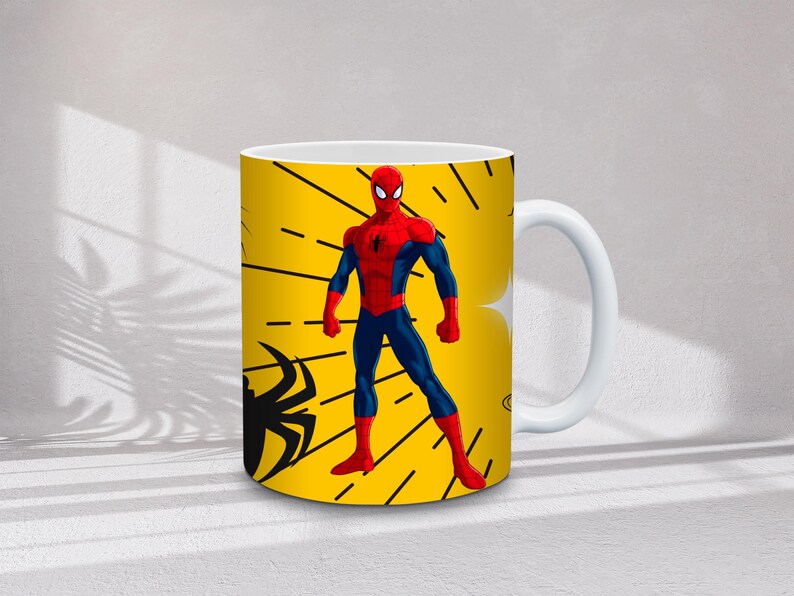 May include: White ceramic mug featuring a vibrant yellow background with a Spider-Man design. The design includes a Spider-Man figure in a red and blue suit, along with black spider silhouettes and web-like lines.