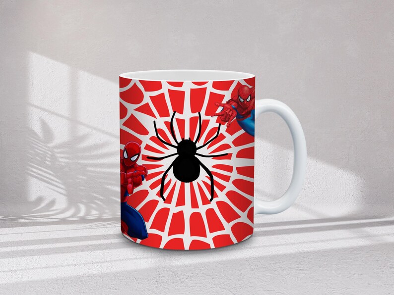 May include: White ceramic mug featuring a red and white spiderweb design with a black spider in the center. The mug also features illustrations of Spider-Man in his red and blue suit.