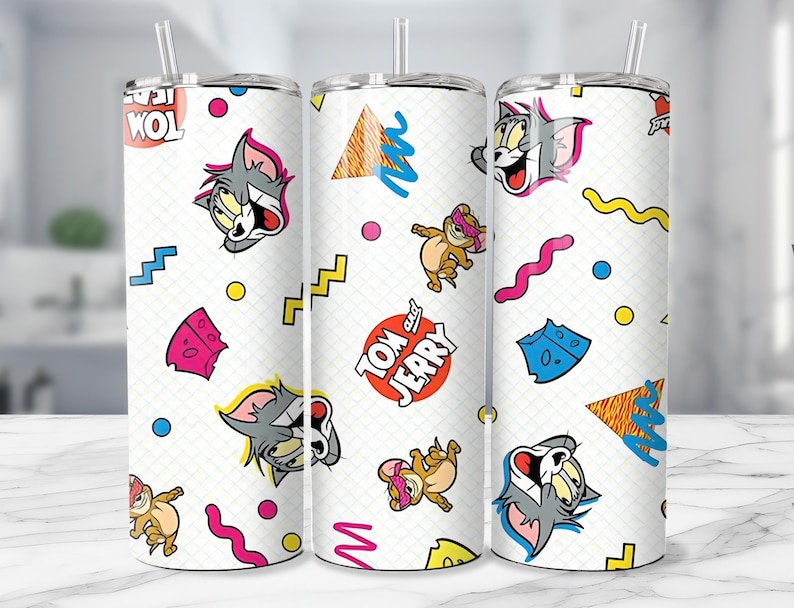 May include: White tumbler featuring a repeating pattern of Tom and Jerry cartoon characters, cheese, and geometric shapes in bright colors. The tumbler includes a straw and the words "Tom" and "Jerry".