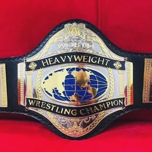 May include: A black leather championship wrestling belt featuring a large central gold and silver plate with a globe graphic and the text WWF WORLD HEAVYWEIGHT WRESTLING CHAMPION. Side plates display the flags of the United States, Mexico, UK, and Australia.