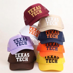 Puede incluir: Una pila de gorras de camionero en varios colores, incluyendo granate, beige, blanco, azul marino, morado, marrón, naranja y amarillo. Cada gorra presenta el texto "TEXAS TECH" en un color contrastante.