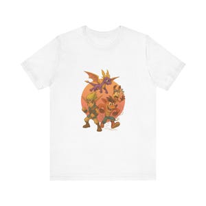 May include: White t-shirt with a cartoon graphic of video game characters set against an orange sun. The design features a purple dragon, a fox-like creature, and two human-like figures in action poses. The graphic is centrally placed on the shirt.