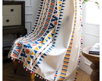 Peut inclure: Rideau crème avec un motif géométrique bleu, orange et jaune. Le motif comprend des triangles, des zigzags et des cercles. Le bord est orné de pompons colorés, ajoutant une touche ludique au traitement de fenêtre.