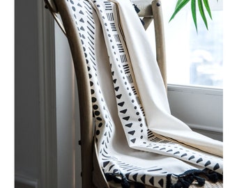Peut inclure: Jeté de canapé blanc et noir à motifs géométriques avec des glands noirs. La couverture est drapé sur une chaise en bois.