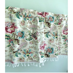 May include: A white valance with a floral pattern in shades of pink, green, and blue. The valance has a white fringe trim.