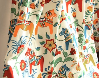 Peut inclure: Tissu blanc avec un motif répété de chevaux stylisés colorés et de fleurs. Les chevaux sont orange, rouge, bleu et vert. Les fleurs sont rouges, orange, jaunes et vertes.