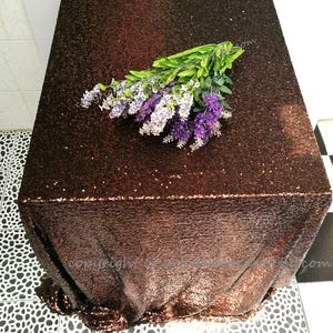 May include: A brown sequined tablecloth with a bouquet of purple and white flowers on top.