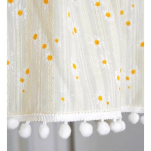 Op de afbeelding: Witte rok met een wit en geel madeliefjespatroon en een witte pomponrand.