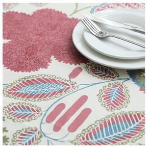 May include: A floral tablecloth with a cream background and a pattern of pink and blue leaves and flowers. Two white plates, a fork, and a knife are on the tablecloth, suggesting a dining setting.