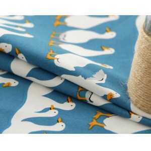 May include: Blue fabric with a white goose pattern. The geese are facing right and have orange beaks and feet.
