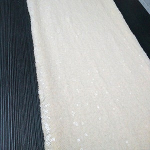 May include: A close-up of a white fabric with small, white sequins. The fabric is smooth and has a subtle sheen.
