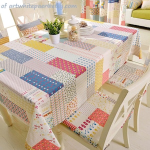 Peut inclure: Une nappe de patchwork avec une variété de couleurs et de motifs, notamment rouge, jaune, bleu et vert. La nappe est posée sur une table avec des chaises blanches.