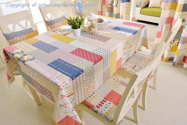 K&ouml;nnte beinhalten: Eine Patchwork-Tischdecke mit verschiedenen Farben und Mustern, darunter Rot, Gelb, Blau und Gr&uuml;n. Die Tischdecke liegt auf einem Tisch mit wei&szlig;en St&uuml;hlen.