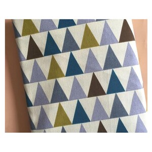May include: A patterned fabric featuring a repeating design of triangles in various shades of blue, brown, and green against a white backdrop. The geometric shapes are arranged in a grid-like pattern. The fabric has a textured appearance, possibly cotton or linen.