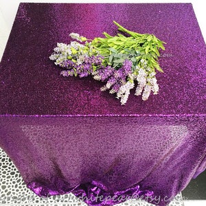 Könnte beinhalten: Lilafarbener Sequinentischläufer mit einem Strauß Lavendelblüten darauf. Der Tischläufer ist aus einem glitzernden Material gefertigt und hat einen dezenten Ombre-Effekt.