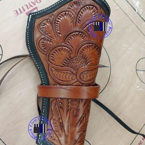 Pode incluir: Uma coldre de couro castanho com intrincados desenhos florais e de folhas. Possui uma borda preta com costura branca e uma presilha de cinto castanha. Uma correia preta est&aacute; presa. O texto "Lion Black Brand" &eacute; vis&iacute;vel.