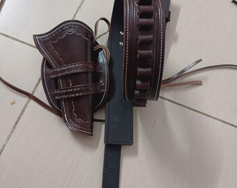 May include: A brown leather gun holster and cartridge belt set. The holster features decorative stitching and a curved design. The cartridge belt is dark brown with multiple loops for bullets. The set is designed for a Western-style look.