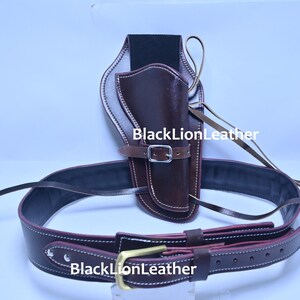 Puede incluir: Un conjunto de cinturón y funda de cuero marrón. La funda está diseñada para sujetar un arma de fuego y está unida a un cinturón a juego. El cinturón tiene una hebilla y está diseñado para usarse alrededor de la cintura. El texto "BlackLionLeather" es visible.