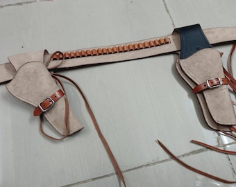 May include: A tan leather gun belt with two holsters and a row of bullet loops. The holsters have brown leather straps and buckles. The belt is made of light tan leather.