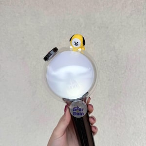 Op de afbeelding: Een zwart-witte lichtstaaf met een heldere, ronde kop en een klein geel stripfiguur erop. Op de lichtstaaf staat het woord "ARMY" gedrukt en een sticker met de tekst "Star Rain".