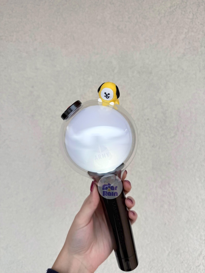 Op de afbeelding: Een zwart-witte lichtstaaf met een heldere, ronde kop en een klein geel stripfiguur erop. Op de lichtstaaf staat het woord "ARMY" gedrukt en een sticker met de tekst "Star Rain".