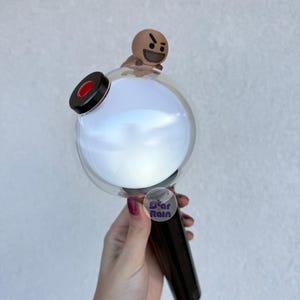 Op de afbeelding: Een zwarte en heldere lichtstaaf met een ronde, gloeiende witte bol en een klein bruin karakter bovenop. De handgreep is zwart en een sticker met de tekst "Star Rain" is zichtbaar.