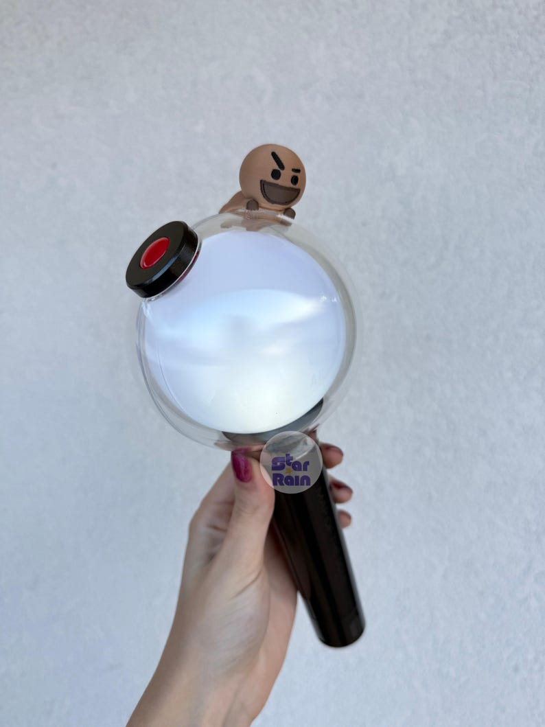 Op de afbeelding: Een zwarte en heldere lichtstaaf met een ronde, gloeiende witte bol en een klein bruin karakter bovenop. De handgreep is zwart en een sticker met de tekst "Star Rain" is zichtbaar.