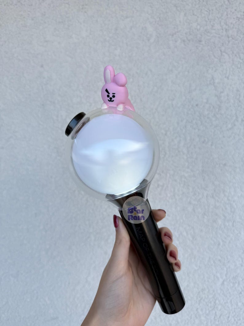 Op de afbeelding: Een zwart-witte lichtstaaf met een heldere bol en een roze konijnenfiguur erop. De handgreep is zwart en de bol is wit. Een kleine sticker met tekst is zichtbaar op de handgreep.