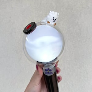 Op de afbeelding: Een witte en heldere lichtstaaf met een ronde kop en een zwarte handgreep. Een klein wit stripfiguur met een bruine vlinderdas zit bovenop de lichtstaaf. De tekst "Star Rain" staat op een sticker op de handgreep.