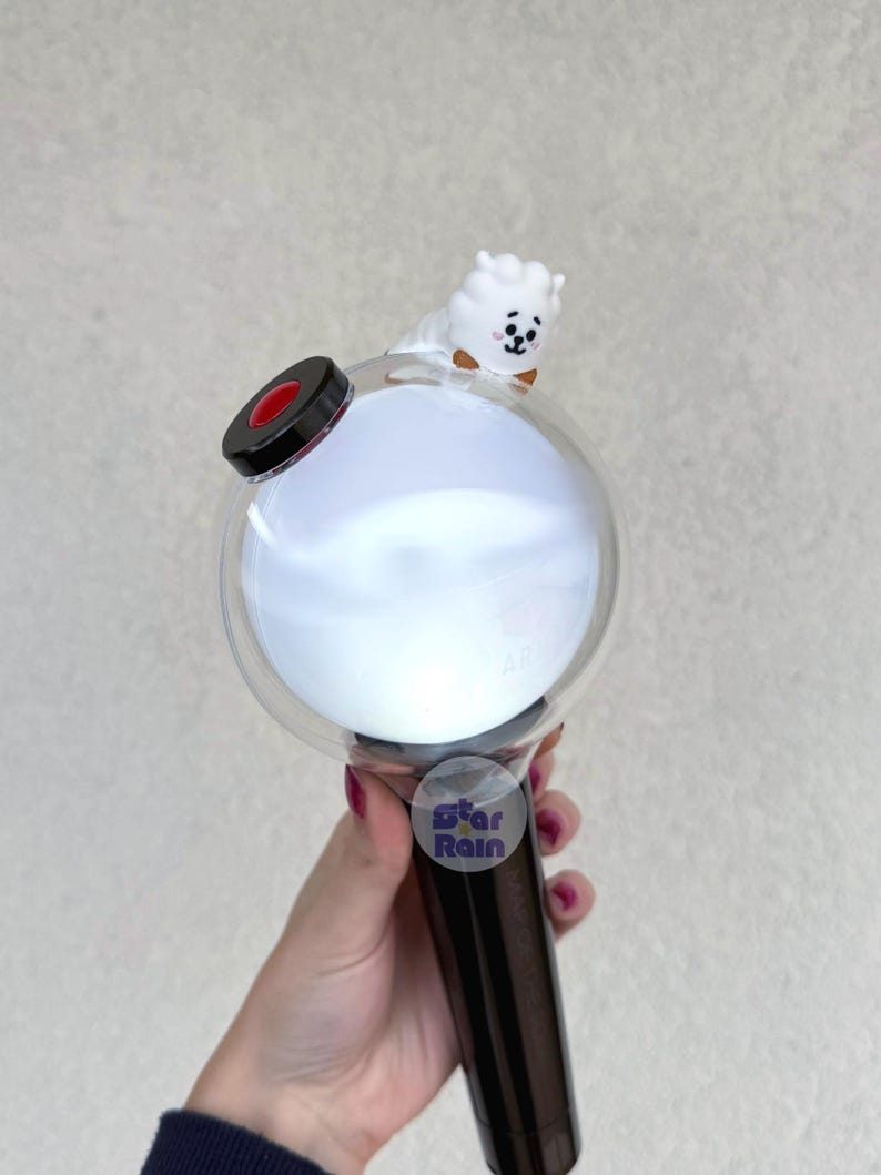 Op de afbeelding: Een witte en heldere lichtstaaf met een ronde kop en een zwarte handgreep. Een klein wit stripfiguur met een bruine vlinderdas zit bovenop de lichtstaaf. De tekst "Star Rain" staat op een sticker op de handgreep.