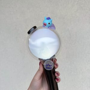 Op de afbeelding: Een zwart-witte lichtstaaf met een heldere bol en een klein blauw stripfiguur erop. Op de lichtstaaf staat het woord "ARMY" gedrukt op de bol en een "Star Rain" sticker op de handgreep.