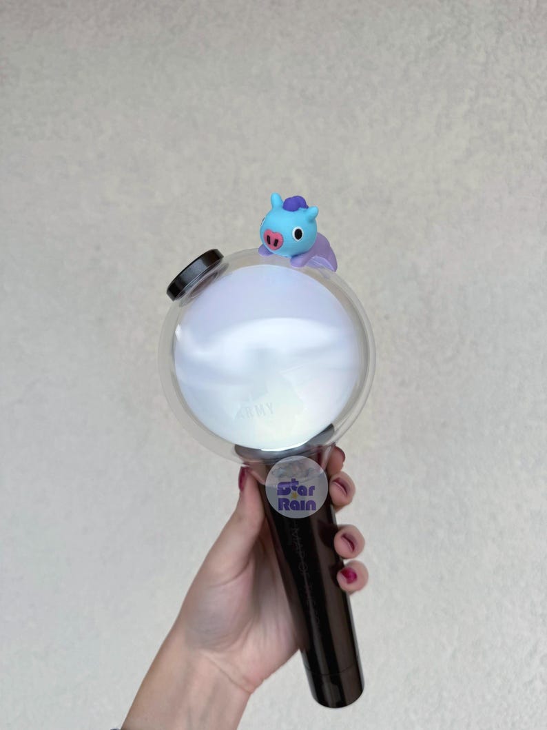Op de afbeelding: Een zwart-witte lichtstaaf met een heldere bol en een klein blauw stripfiguur erop. Op de lichtstaaf staat het woord "ARMY" gedrukt op de bol en een "Star Rain" sticker op de handgreep.