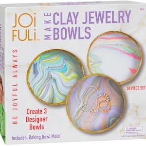 May include: A craft kit for making clay jewelry bowls. The box features three finished bowls with colorful, marbled designs and gold rims. Text on the box reads "CLAY JEWELRY BOWLS" and "Create 3 Designer Bowls". The kit includes a baking bowl mold and is a 28-piece set.