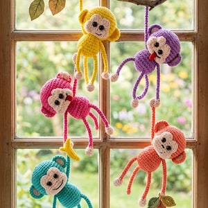 May include: A collection of five colorful, crocheted monkey ornaments hanging from a wooden branch in front of a window. The monkeys are yellow, purple, pink, teal, and orange, each with a unique expression and holding a banana or leaves.