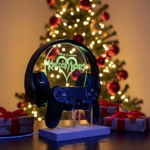 May include: A black gaming headset and controller are displayed on a stand with a glowing Kingdom Hearts logo. The stand is on a wooden base, with a Christmas tree and wrapped gifts in the background.