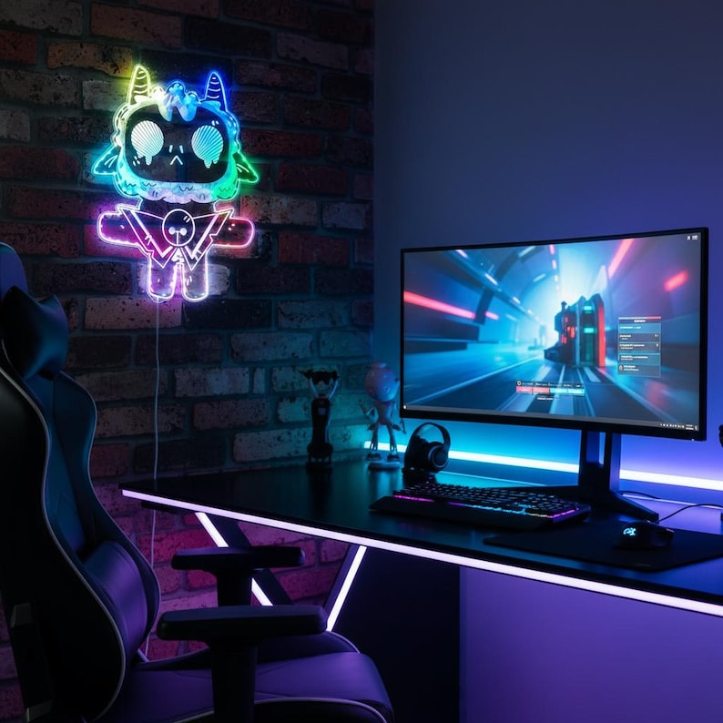 May include: A gaming setup with a neon light fixture in the shape of a cartoon character on a brick wall. The desk has a monitor, keyboard, and mouse. A gaming chair is in the foreground. The room is lit with neon lights.