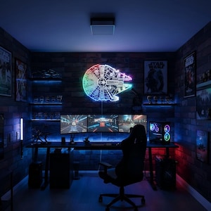 Puede incluir: Una sala de juegos temática de Star Wars. Cuenta con un letrero de neón del Halcón Milenario, múltiples monitores de computadora y una silla de juego. Las paredes son de ladrillo y la habitación está iluminada con luces azules y rojas.