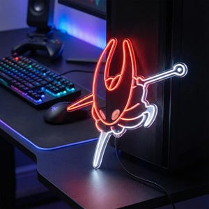 May include: A neon light featuring a red and white stylized character design, mounted on a black computer tower. The light is plugged in and illuminates the character's outline. The desk has a keyboard, mouse, and speaker.