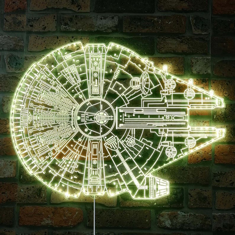 K&ouml;nnte beinhalten: Eine neongr&uuml;ne Millennium Falcon Wandleuchte, die das komplizierte Design des Schiffs zeigt. Die Leuchte ist an einer Backsteinmauer befestigt, was einen auff&auml;lligen Kontrast erzeugt. Der Umriss der Leuchte leuchtet und hebt die Details des Schiffs hervor.