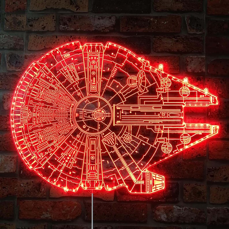 K&ouml;nnte beinhalten: Rotes LED-Licht in Form des Raumschiffs Millennium Falcon. Das Licht zeigt eine detaillierte Umrisszeichnung des Schiffsdesigns mit rotem Leuchten. Das Licht ist an einer Backsteinmauer befestigt.