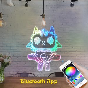 May include: A vibrant, illuminated cartoon character with Bluetooth App control. The character features a distinctive design with horns and a geometric body. The app on the phone displays a colour wheel for customisation. The text "Bluetooth App" is at the bottom.
