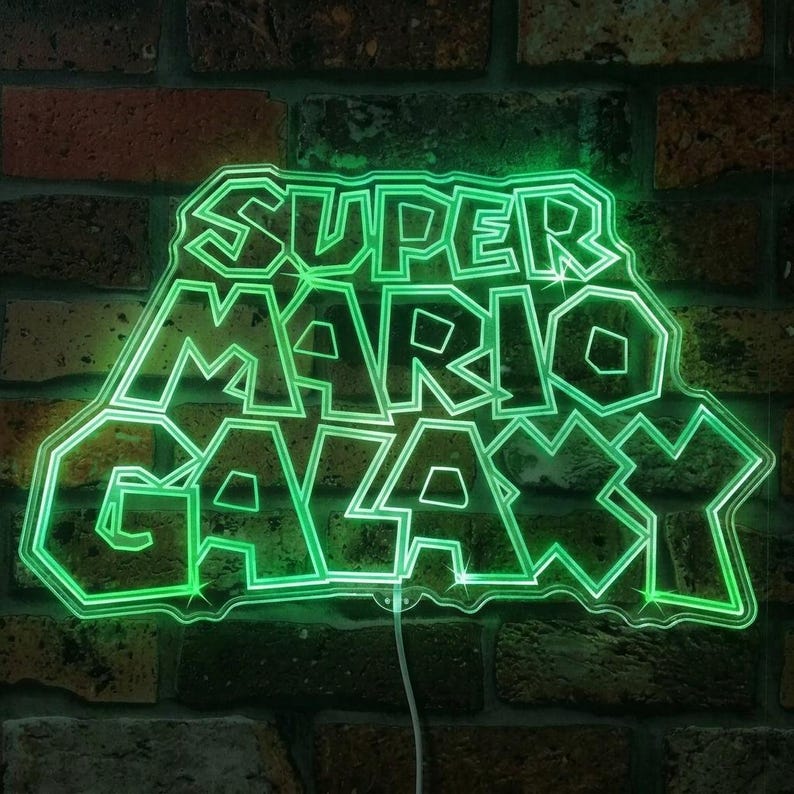 May include: A neon green sign displaying the text "SUPER MARIO GALAXY" in a distinctive font. The sign, outlined in bright green, is mounted on a brick wall. The illuminated sign has a visible power cord.